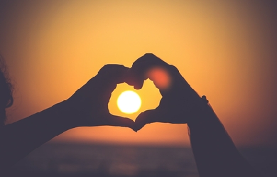 The sun inside a heart made with hands